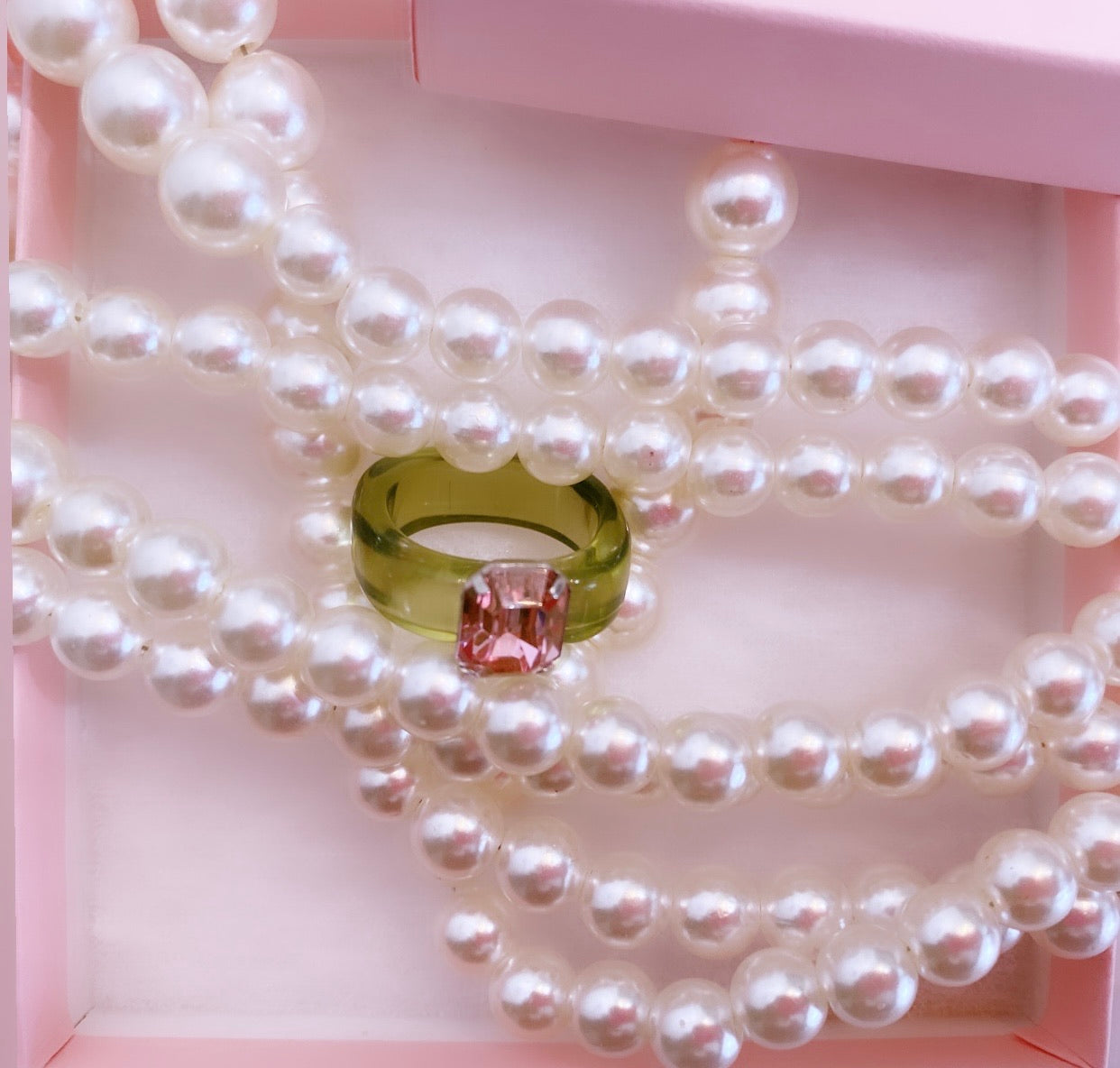 Pink acrylic ring band with green gem paired with a pearl necklace.